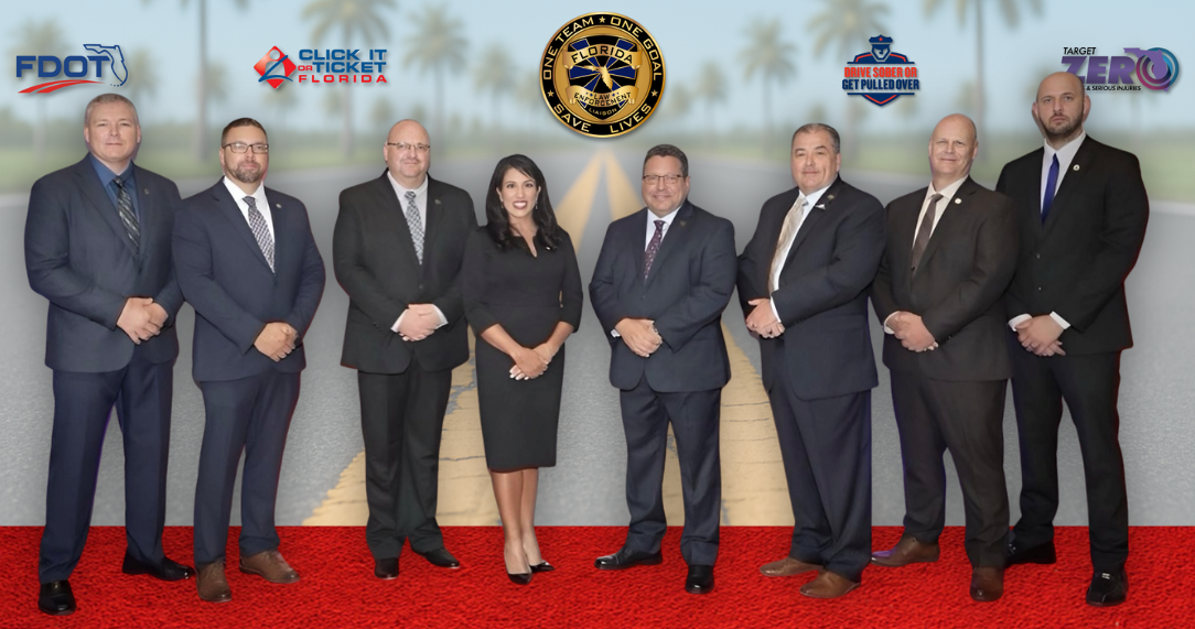 Group of eight professionals, wearing business attire, backdrop displaying traffic safety logos.